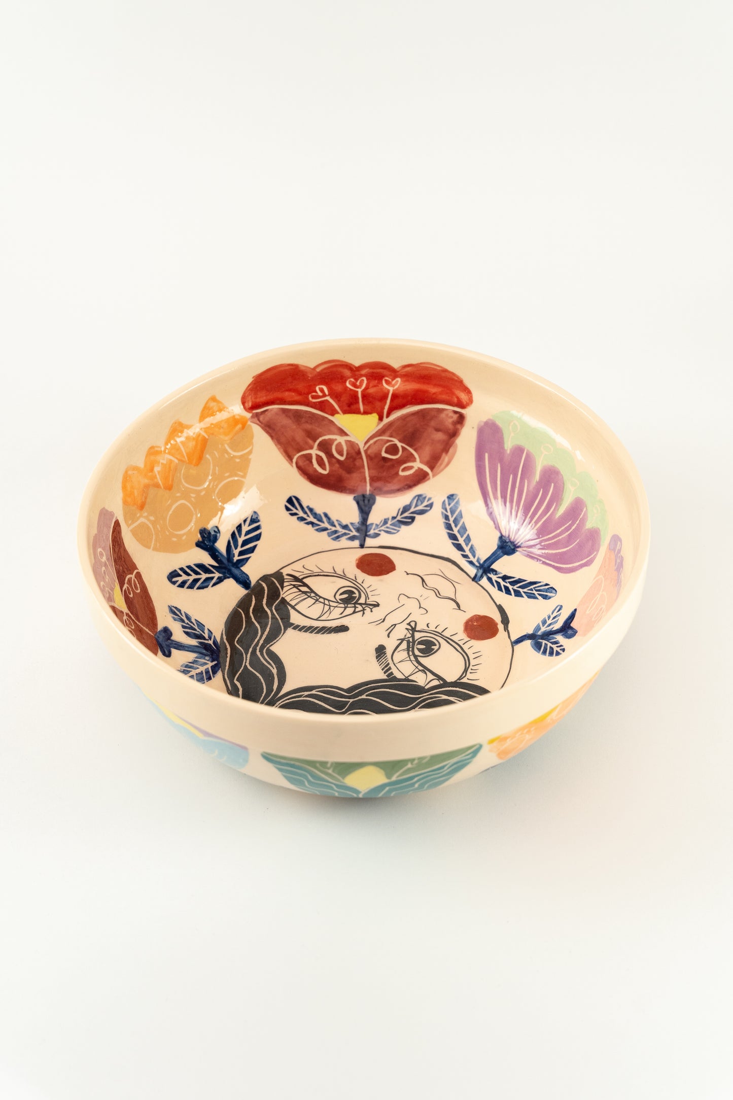 Handmade ceramic serving bowls fpor salads, with colorful flower details and a kind face design on the bottom of the bowl