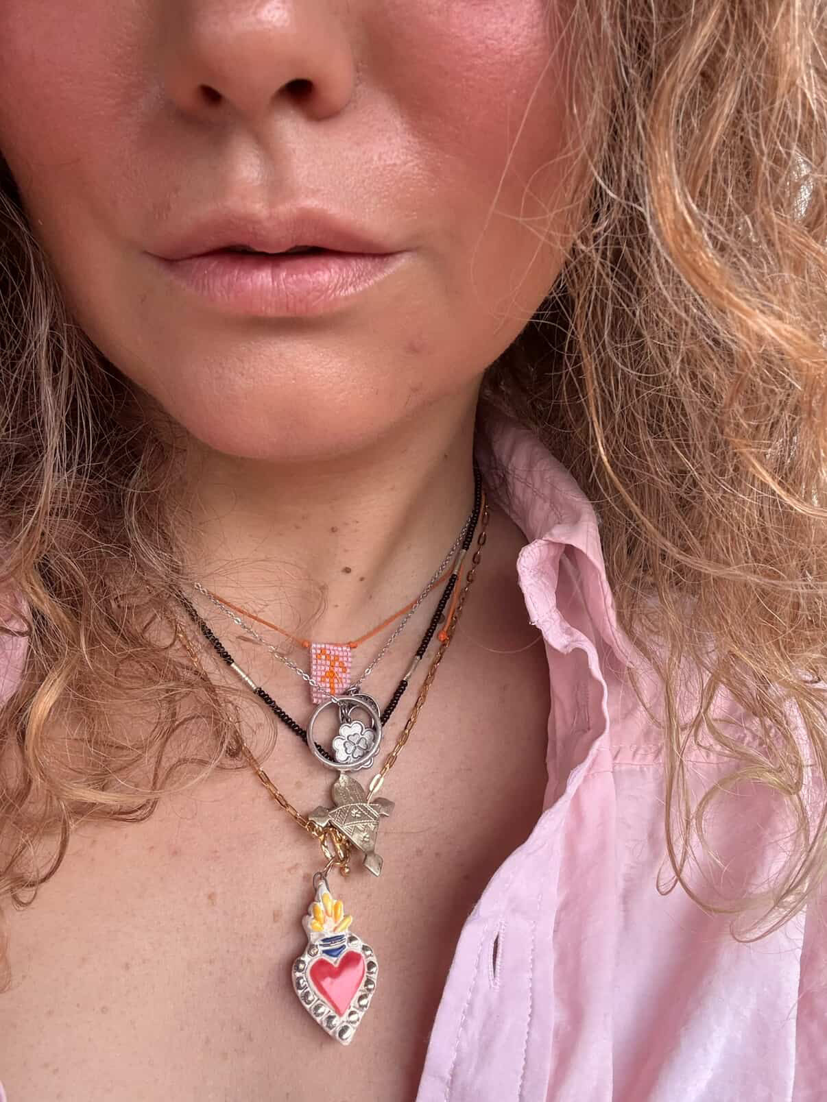 Close-up of a person wearing multiple necklaces with heart-shaped pendants.