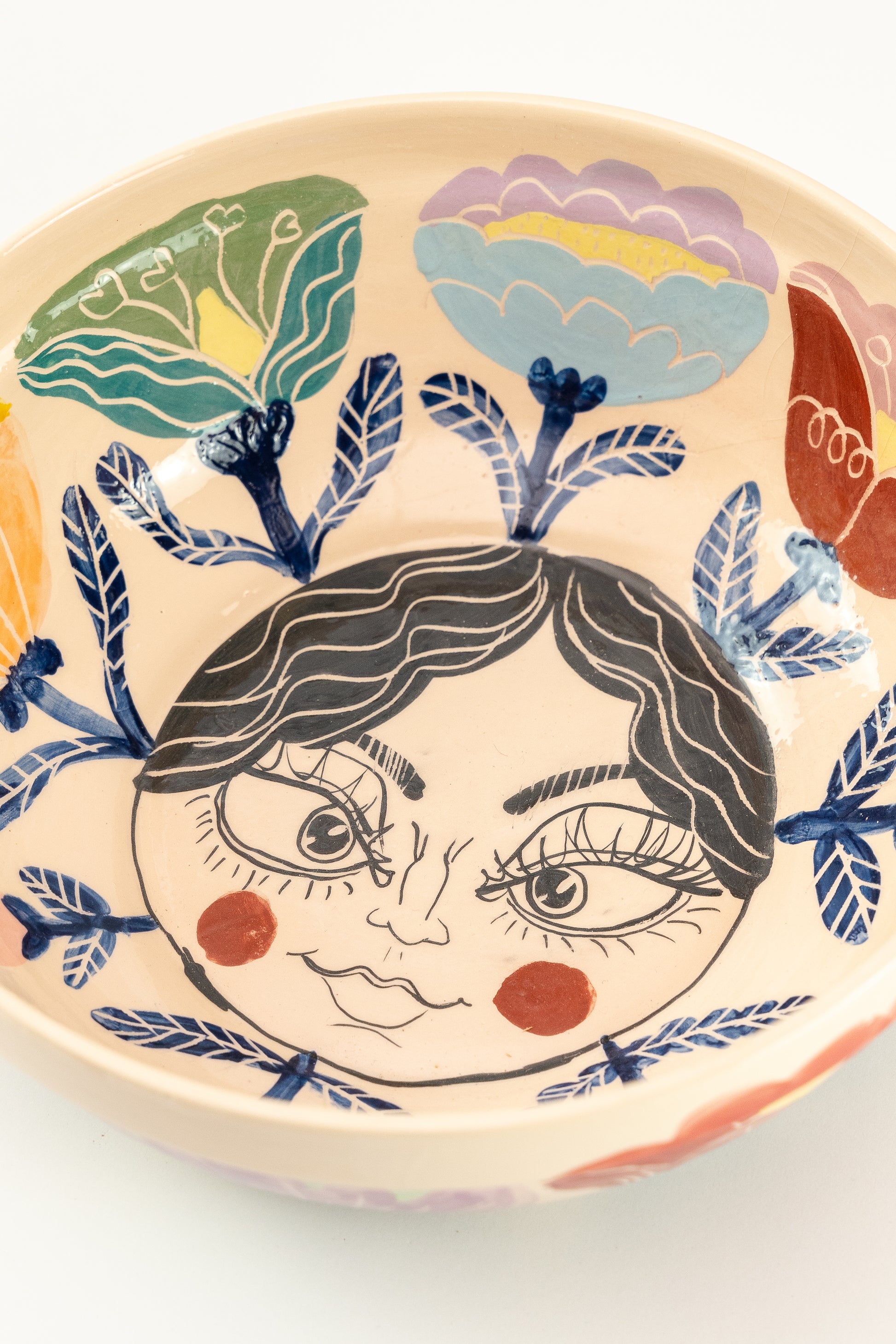 Handmade ceramic serving bowls fpor salads, with colorful flower details and a kind face design on the bottom of the bowl